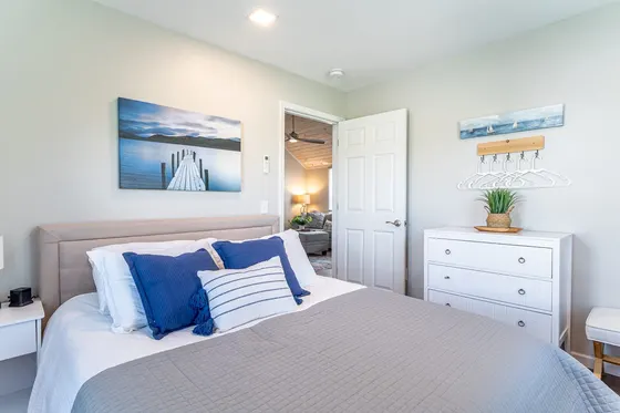 Coastal bedroom with a queen bed, white dresser, and lake artwork.