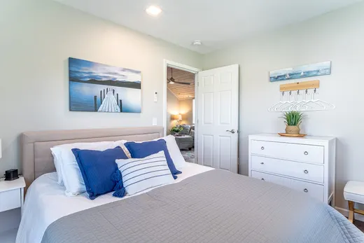 Coastal bedroom with a queen bed, white dresser, and lake artwork.