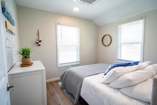 Queen bedroom with a made bed, a dresser, and two windows.