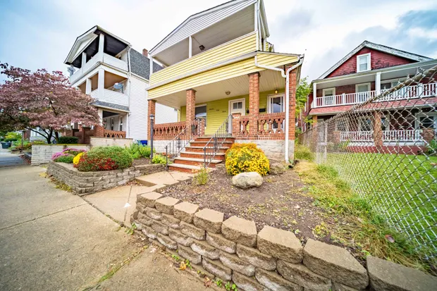 Angled view of the yellow house with its porch, landscaping, and a mature tree.