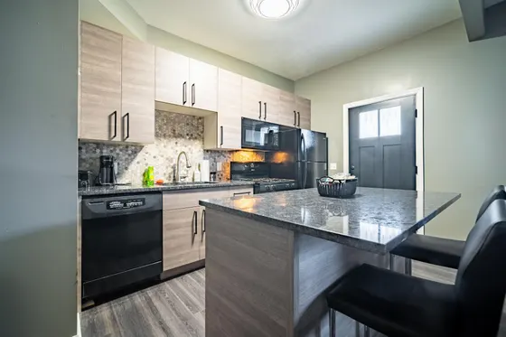 Kitchen island with two black bar stools, light wood cabinets, and black appliances.