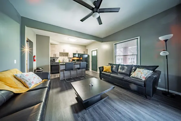 Open-plan living room and kitchen with black leather sofas and light wood cabinets.
