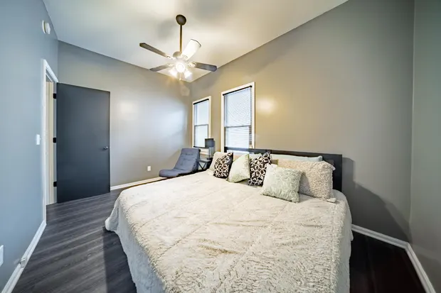 Bedroom with a large bed and white bedding, grey walls, and a ceiling fan.