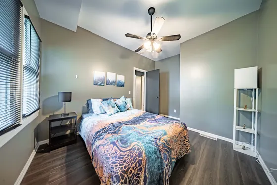Bedroom with a queen bed in vibrant blue and orange swirl bedding and a ceiling fan.