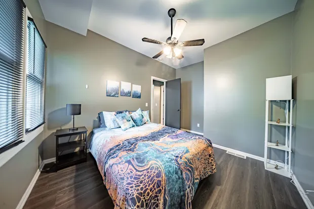 Bedroom with a queen bed in vibrant blue and orange swirl bedding and a ceiling fan.