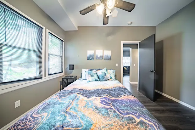 Queen bed with colorful swirl bedding beneath a window with blinds.