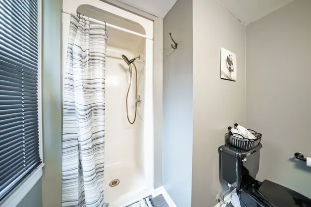 Walk-in shower with a curtain beside a window with blinds.