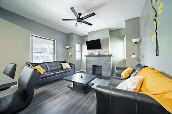 Living room with two black leather sofas, yellow pillows, and a mounted TV.