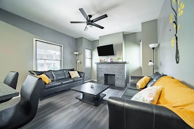 Living room with two black leather sofas, yellow pillows, and a mounted TV.