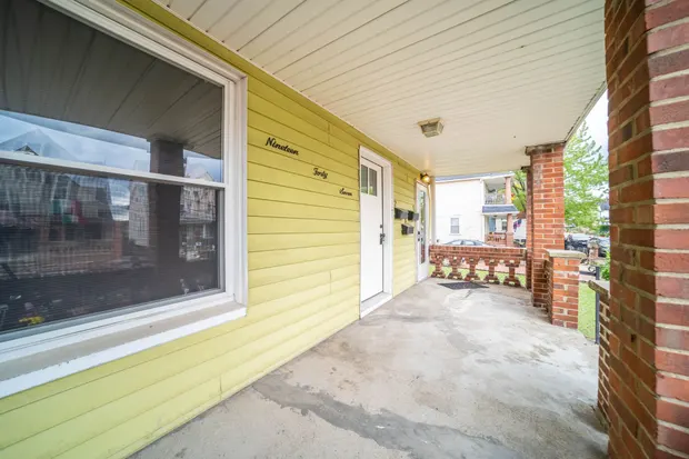 Covered front porch with yellow siding, brick columns, and a wide window.