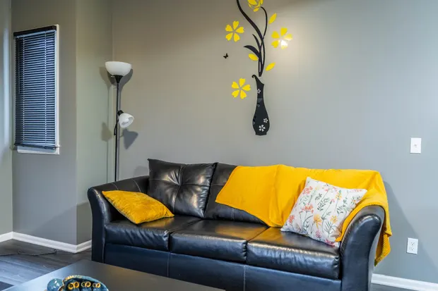 Black leather couch with a yellow throw blanket and patterned accent pillows.