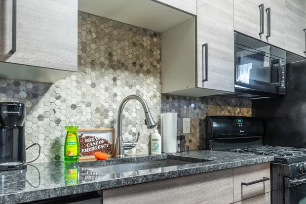Kitchen sink and granite-look counter with a coffee maker and a Little Italy sign.