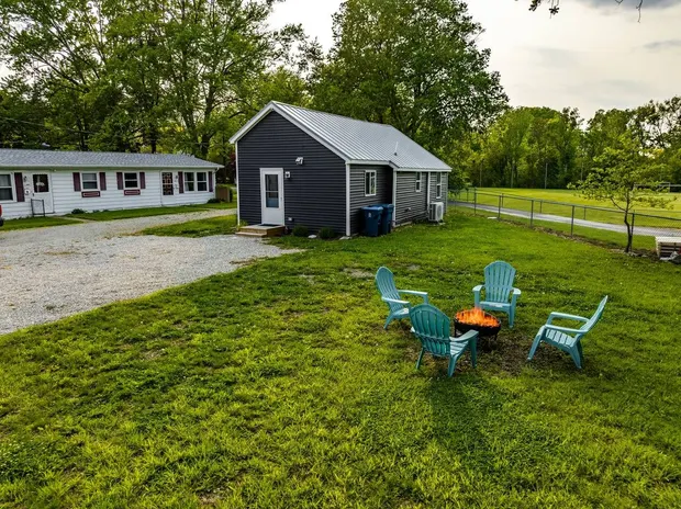 Charcoal cottage with a metal roof seen from the backyard, with a fire pit and Adirondack chairs on the lawn.