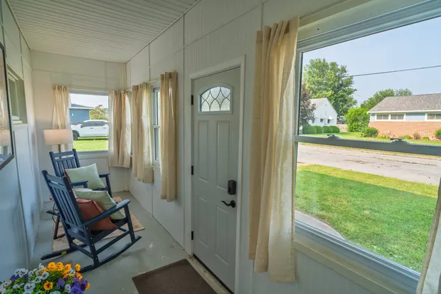 Enclosed front sunroom with navy rocking chairs and windows onto the front yard.