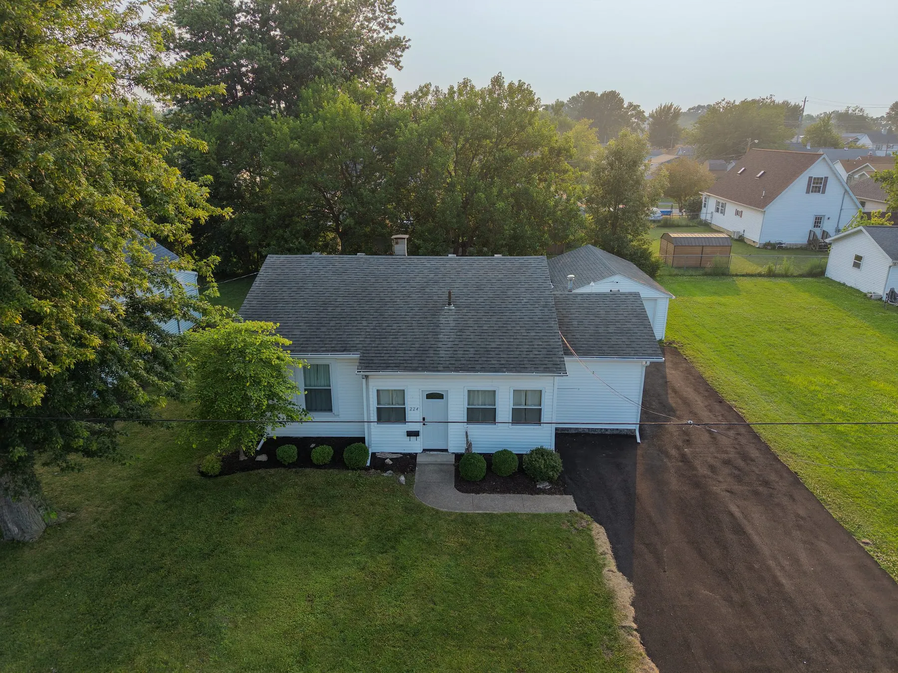 Aerial view of the white single-storey home with a long driveway and green side yard.