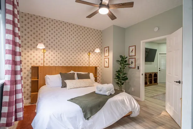 Second king bedroom with cream floral wallpaper, red gingham curtains, and a doorway to the living room.