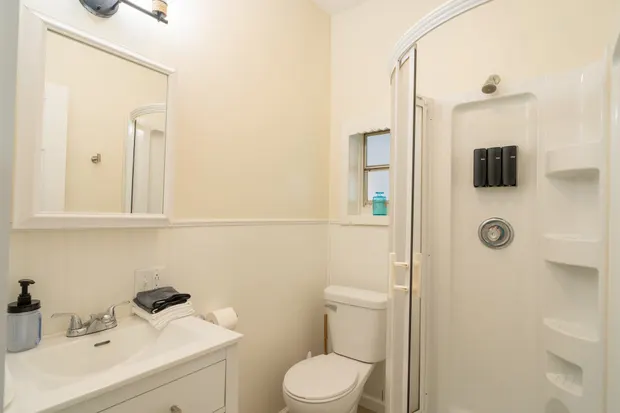 Hallway bathroom with a standup corner shower, toilet, and wall-mounted shampoo, conditioner, and body wash.
