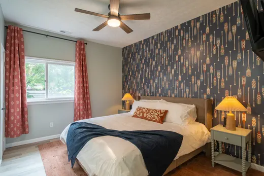 King bedroom with navy paddle-print wallpaper, rust curtains, and a wall-mounted TV.