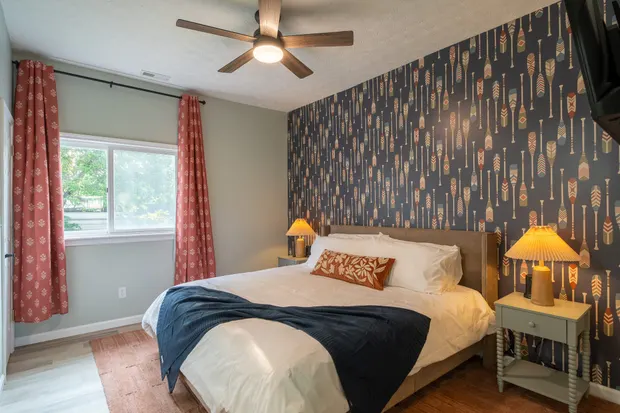 King bedroom with navy paddle-print wallpaper, rust curtains, and a wall-mounted TV.