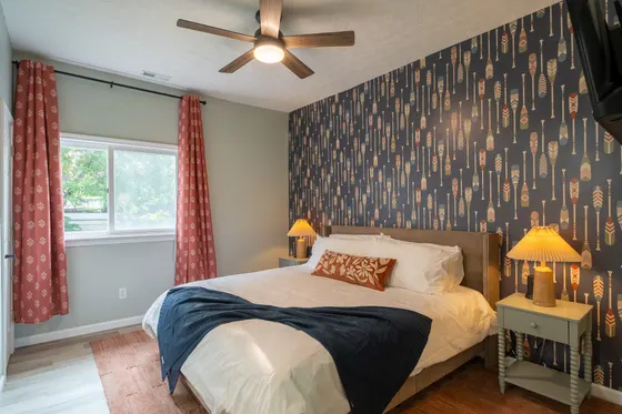 King bedroom with navy paddle-print wallpaper, rust curtains, and a wall-mounted TV.