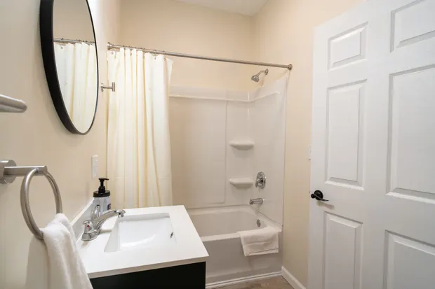 Ensuite bathroom with a tub and shower combo, a vanity, and a round mirror.