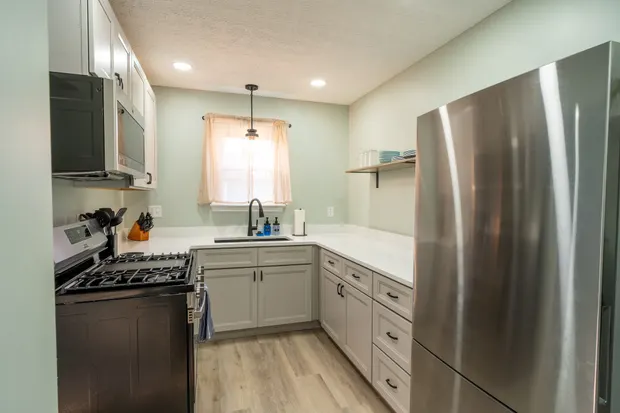 Kitchen with a gas range, stainless refrigerator, and open shelving by the window.