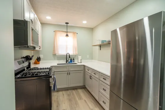 Kitchen with a gas range, stainless refrigerator, and open shelving by the window.