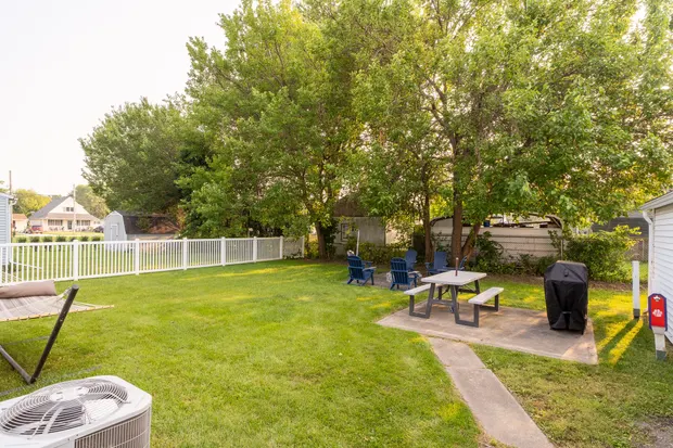 Backyard with a gas grill, a picnic table, and a fire-pit seating area ringed by chairs.