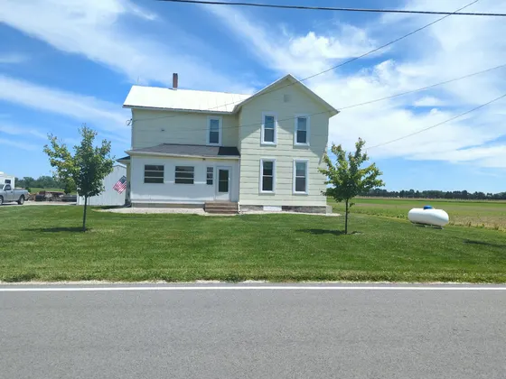 Pale yellow two-storey farmhouse on a green lawn under a blue sky.