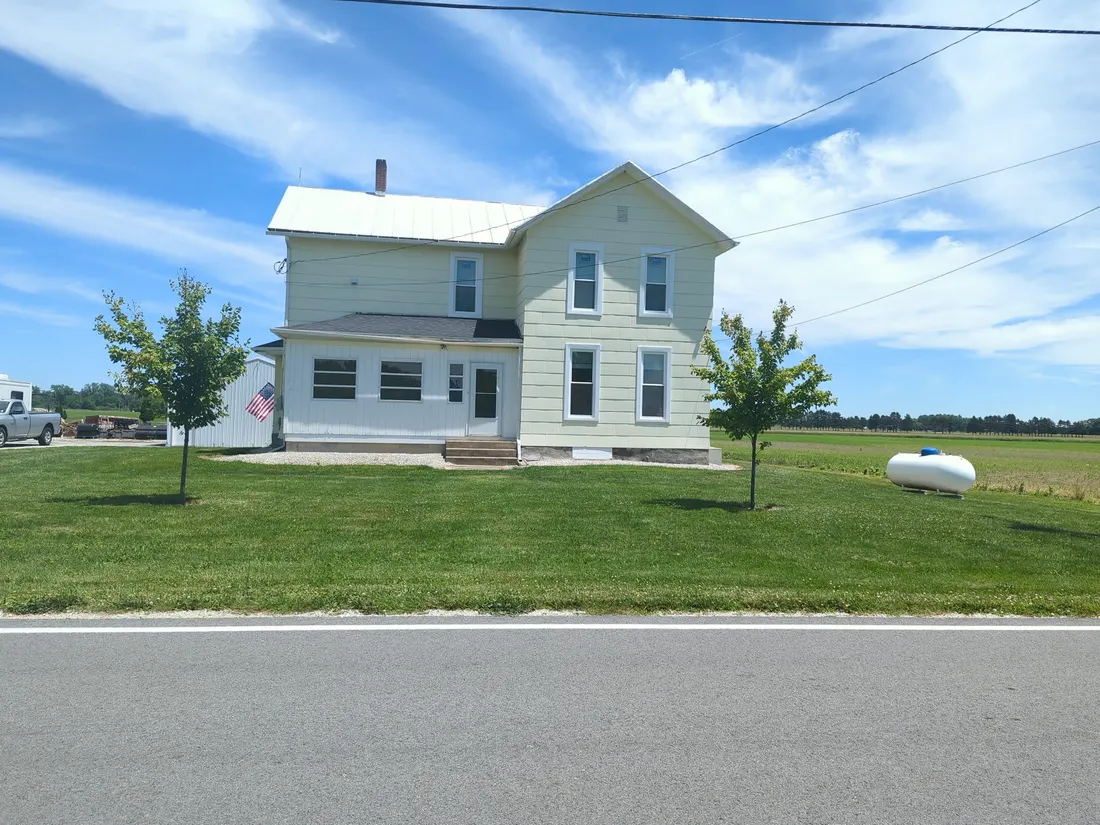 Pale yellow two-storey farmhouse duplex on a green lawn under a blue sky.