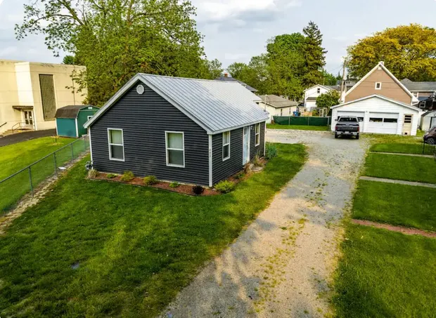 The renovated navy cottage from the gravel drive, with a metal roof and neighbouring homes.