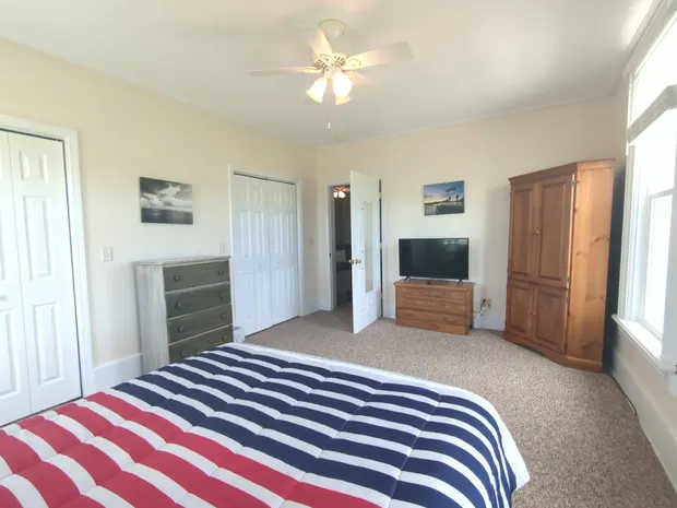 Queen bedroom with striped bedding and two windows.