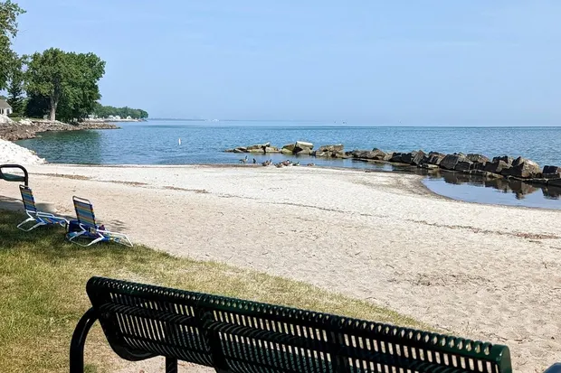 Sandy Lake Erie beach with a rock breakwater, beach chairs, and calm water.
