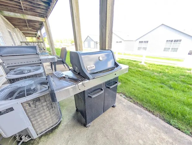 Ground-floor patio with a gas grill beside a grassy lawn.