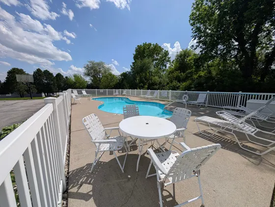 Kidney-shaped outdoor pool with lounge chairs inside a white fence.