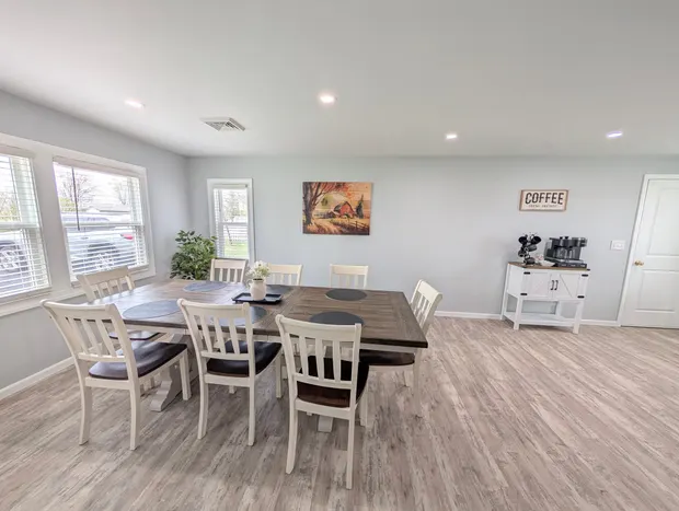 Dining area with a wooden table and white chairs by bright windows.