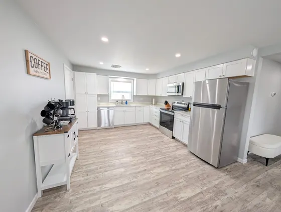 Modern white kitchen with stainless steel appliances and wood floors.