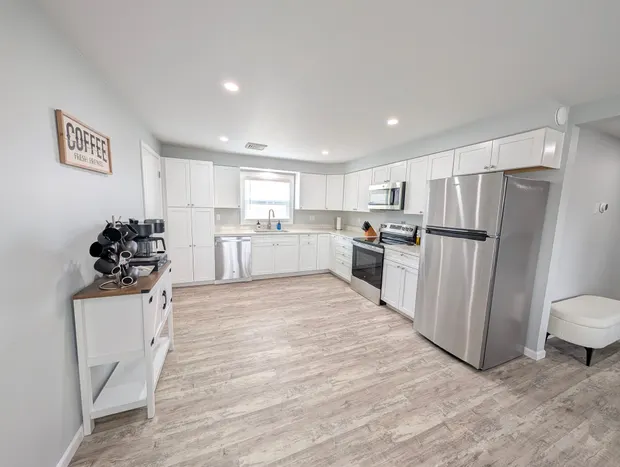 Modern white kitchen with stainless steel appliances and wood floors.