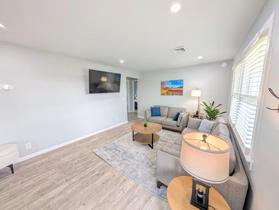 Bright living room with grey sofas, blue pillows, and a wall-mounted TV.