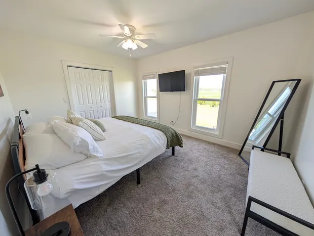 Clean modern bedroom with a bed, TV, and leaning mirror.
