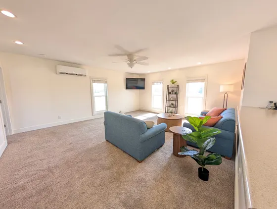 Bright upstairs living room with two blue sofas and a mounted TV.