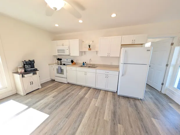 White kitchen with white appliances and grey wood-look floors.